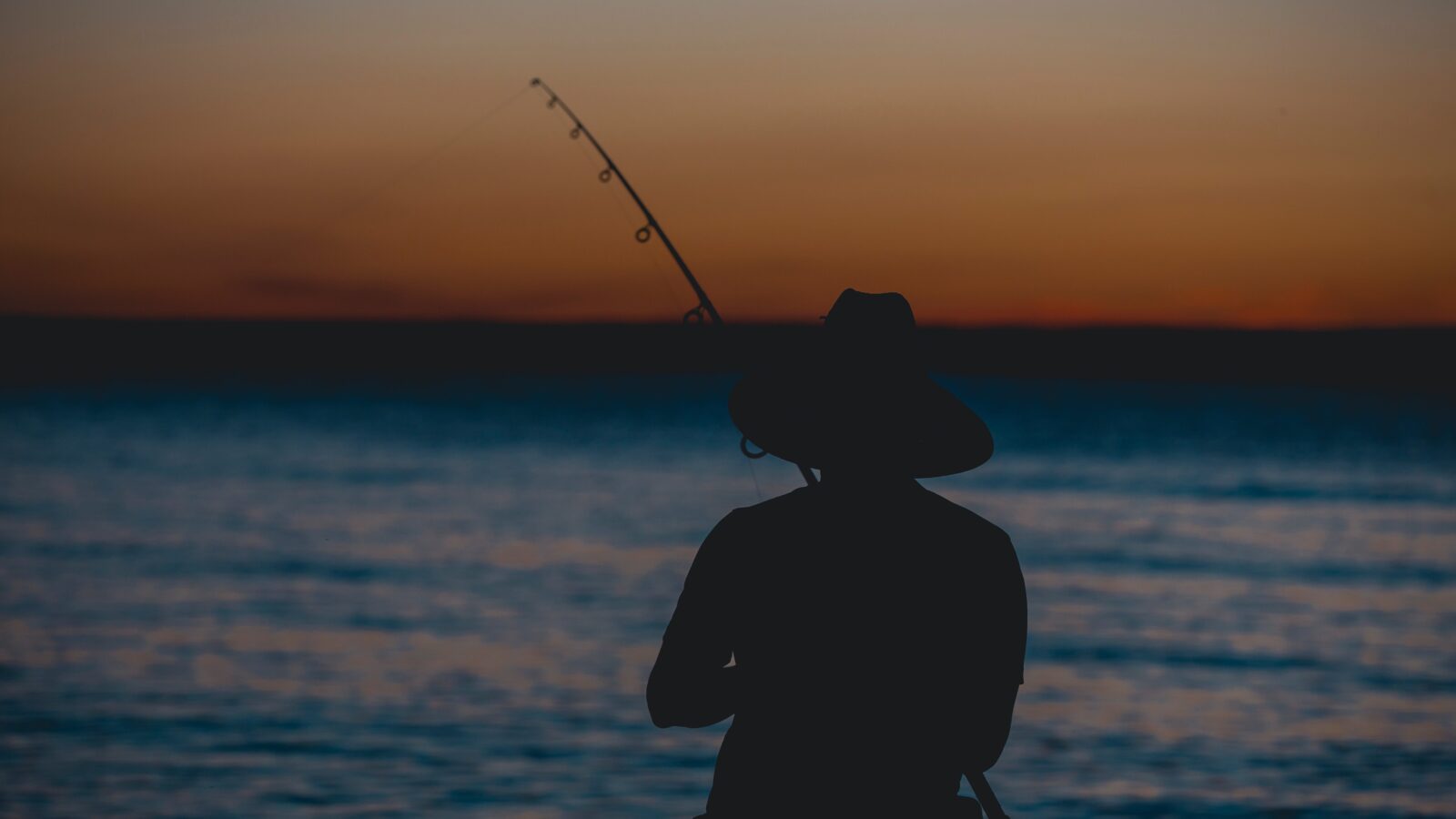 Sun setting over the sea with a silhouette of a fisherman in the foreground